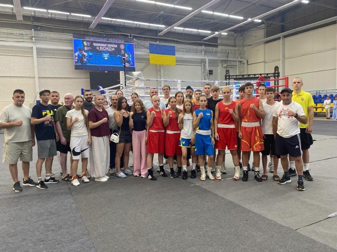 Групове фото юних боксерів, тренерів і представників команд після змагань у спортивному залі на тлі боксерського рингу.