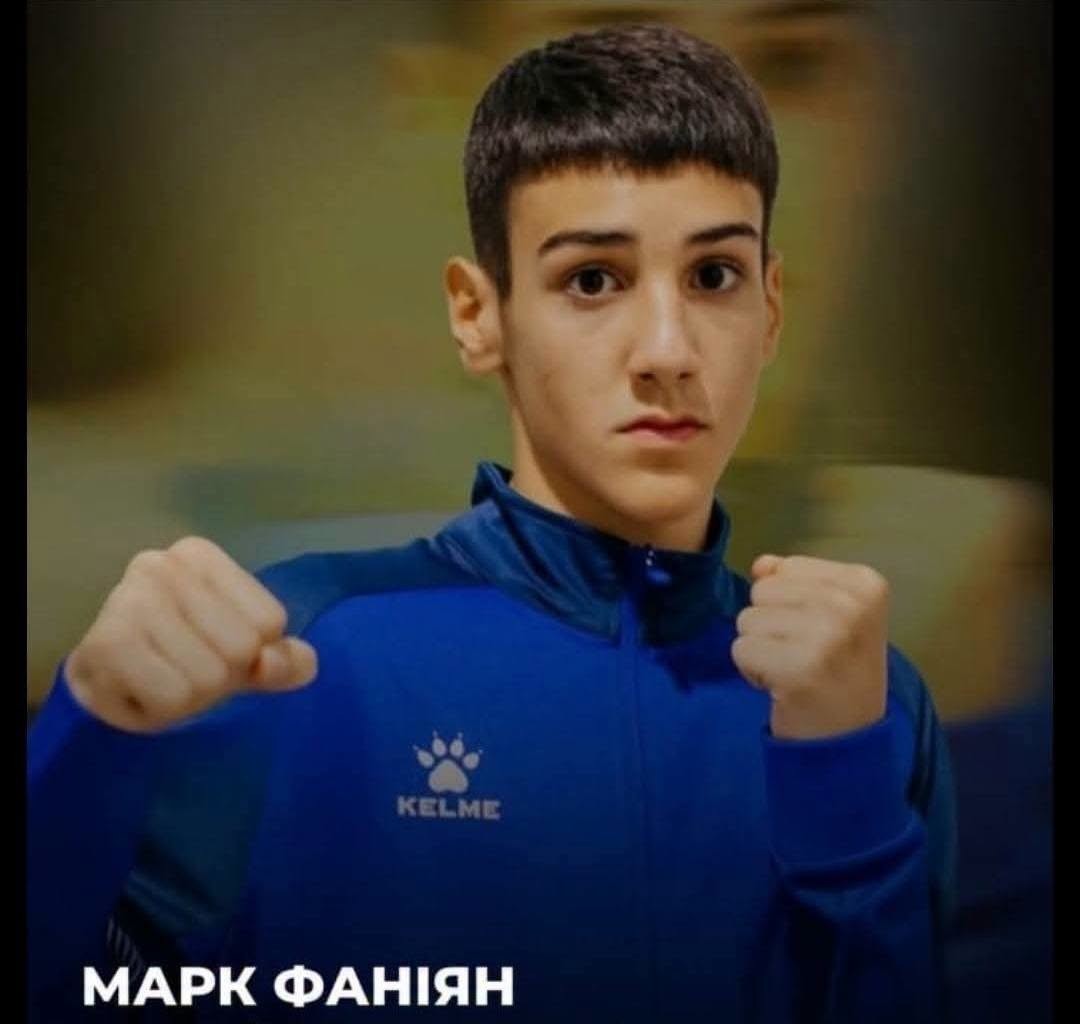 Юний боксер у синій спортивній кофті позує зі стиснутими кулаками перед камерою