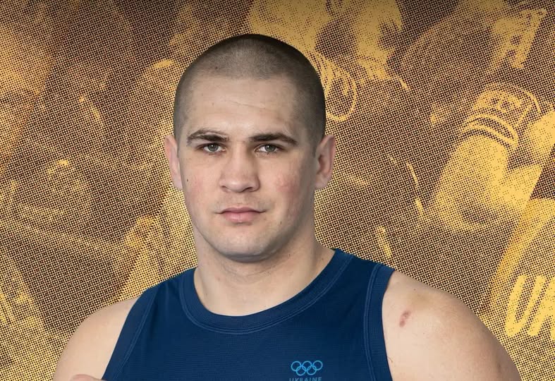 Портрет чоловіка спортивної статури із короткою стрижкою у синій майці з олімпійськими кільцями на тлі золотавого графічного візерунка.