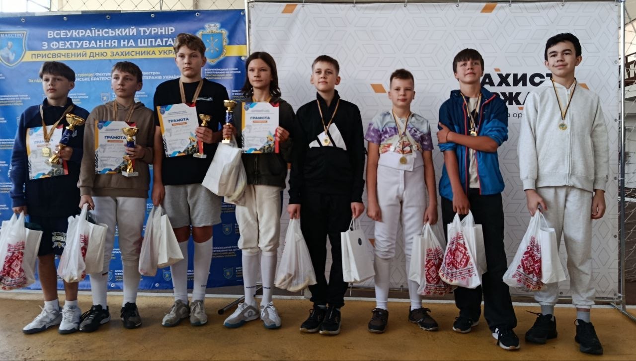 Вісім юних спортсменів стоять у ряд. Дехто тримає кубки, грамоти та білі пакети з подарунками, у всіх на шиях блищать медалі.